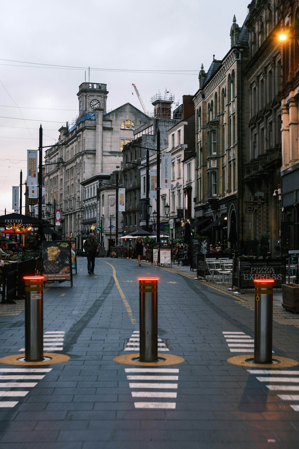 Pedestrians walk along a historic European street with outdoor dining.