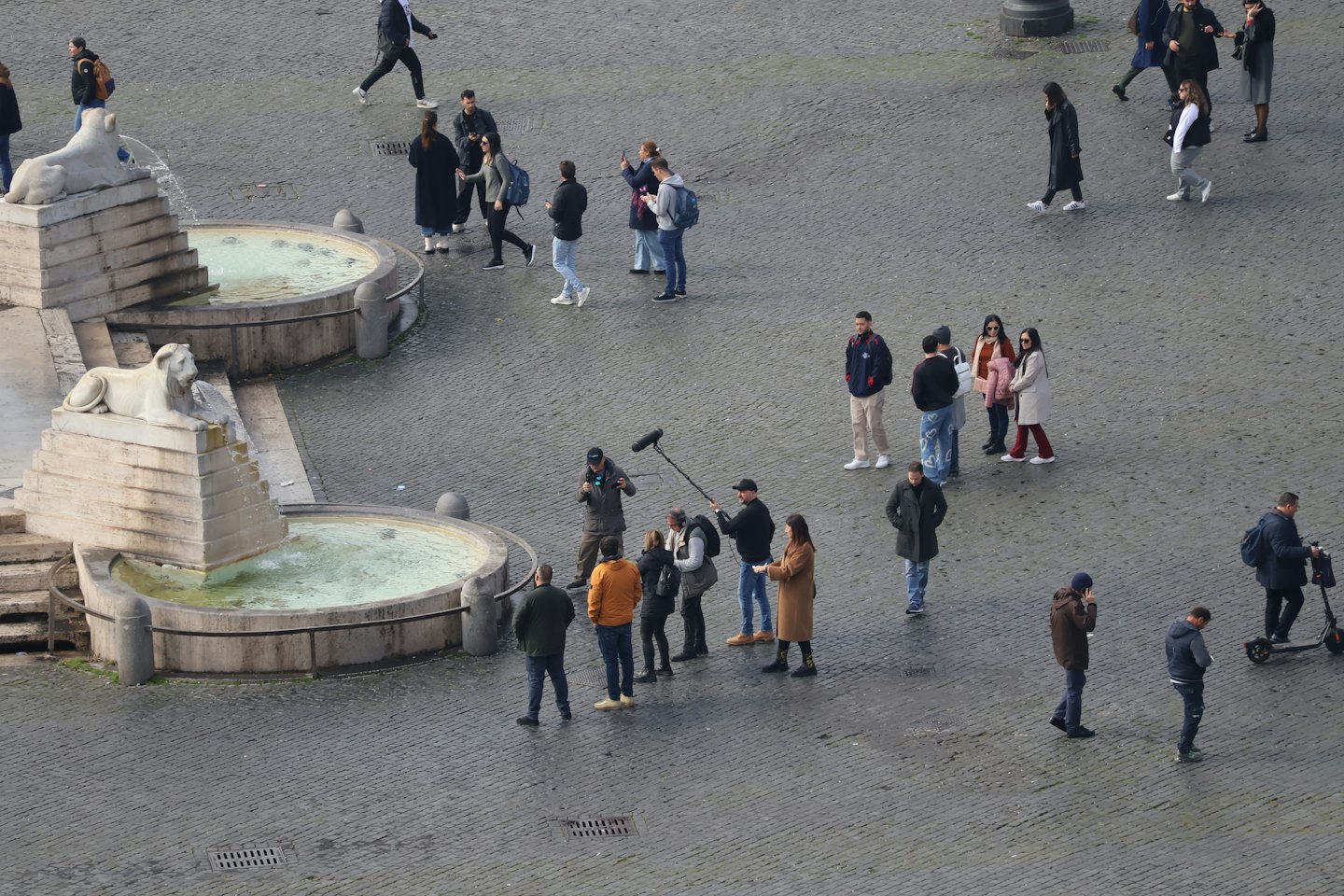 Film crew records a scene in a busy cobblestone square.
