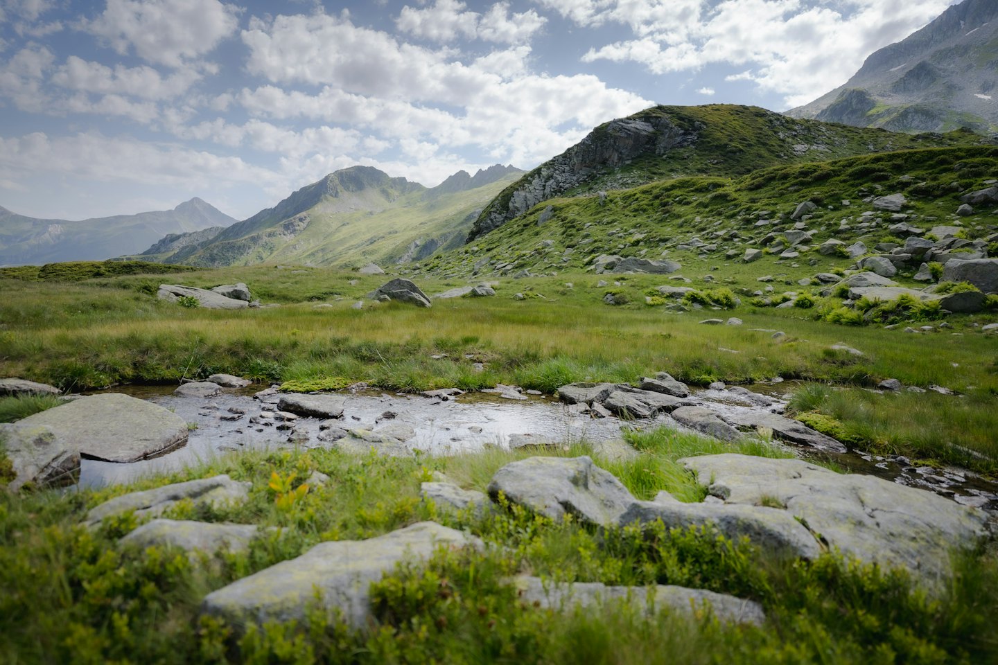 A small rocky stream flows through a lush mountain landscape.