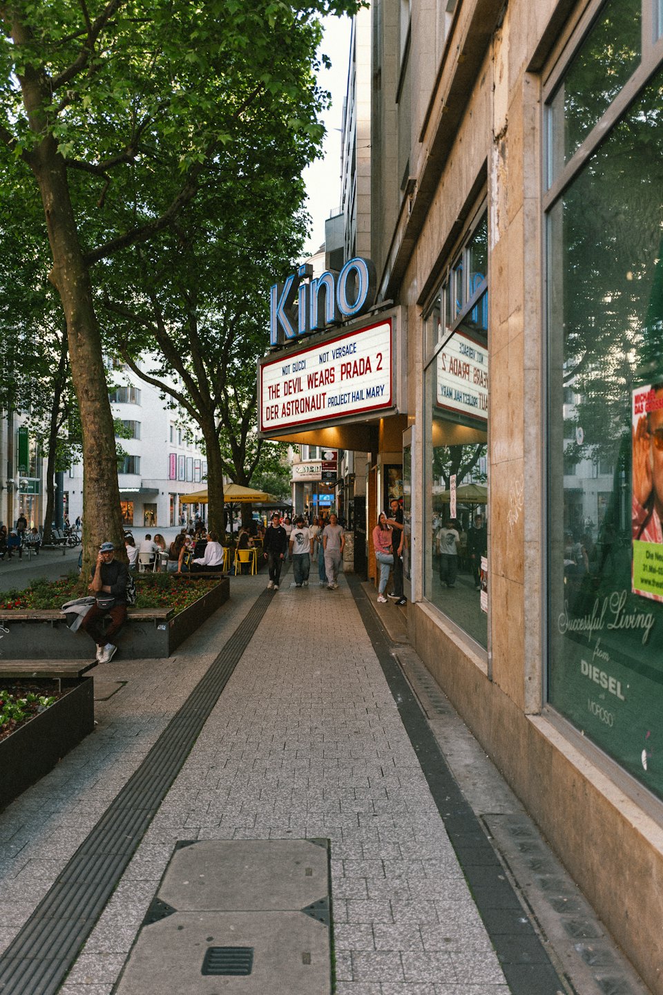 Pedestrians walk past a city cinema with an outdoor cafe.
