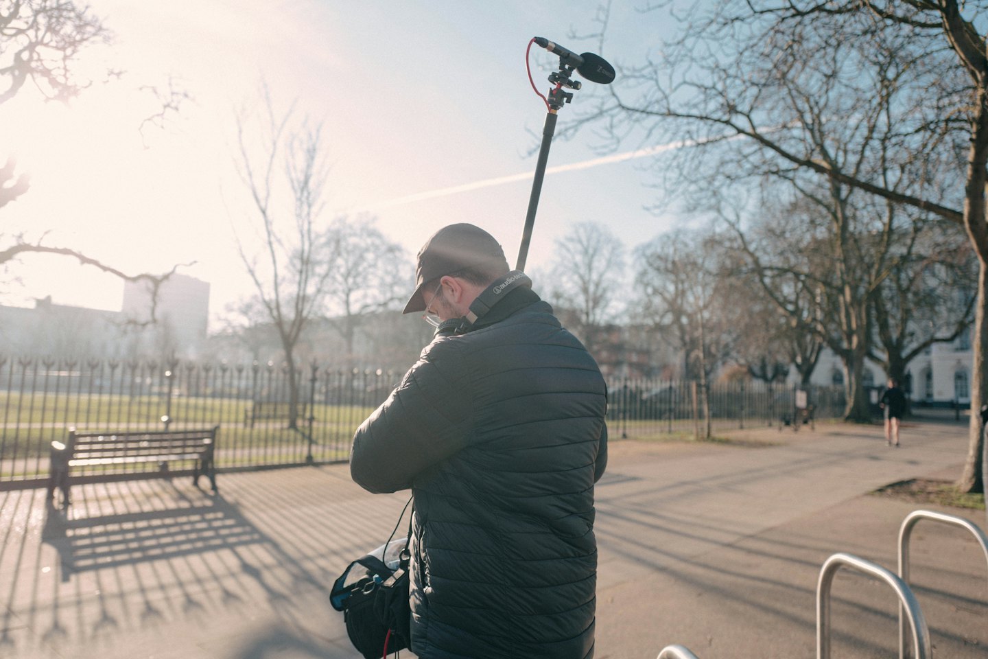 Sound recordist holding a boom microphone in a park.